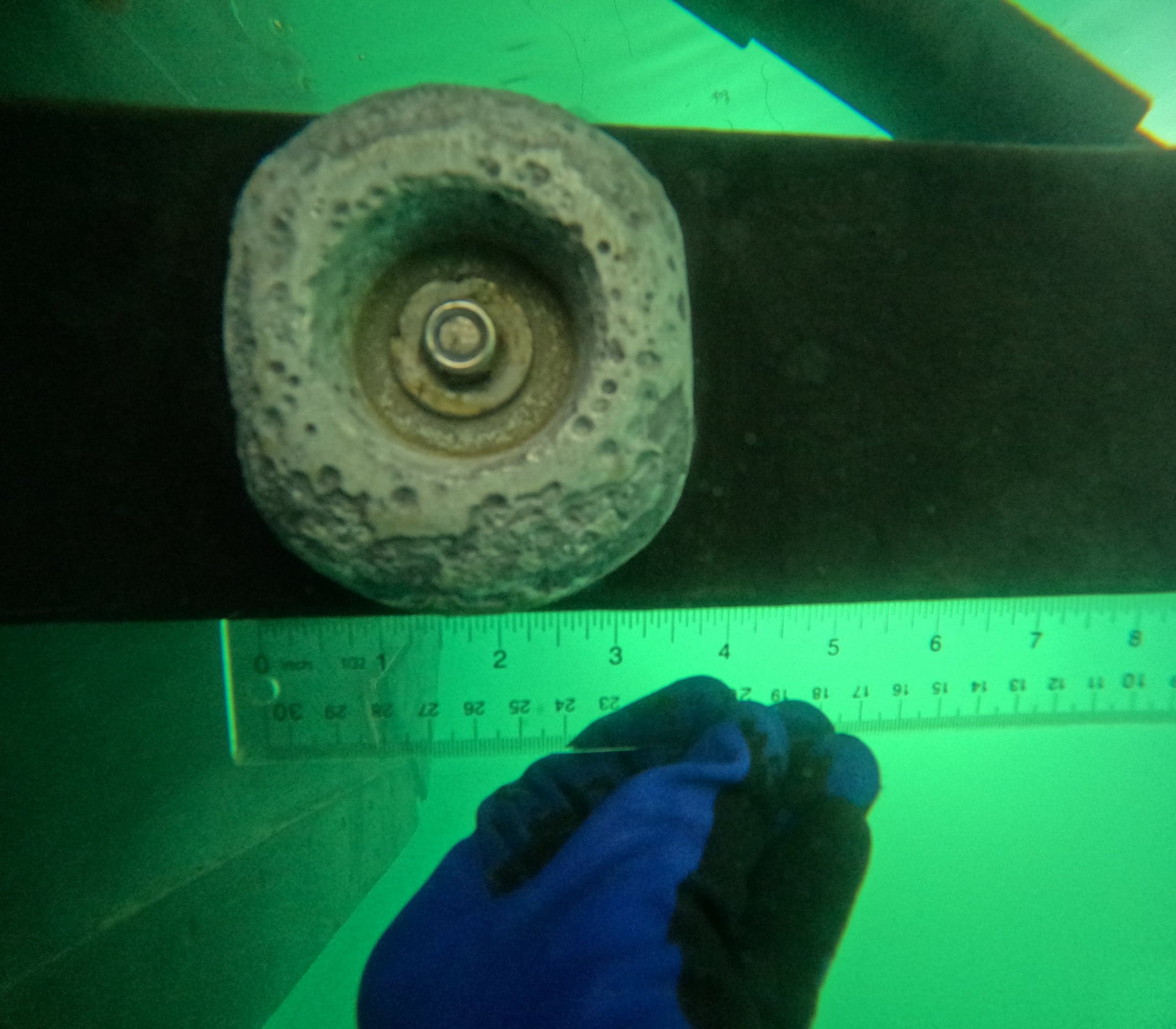 Underwater shaft anode being measured with a ruler, anode visibly depleted