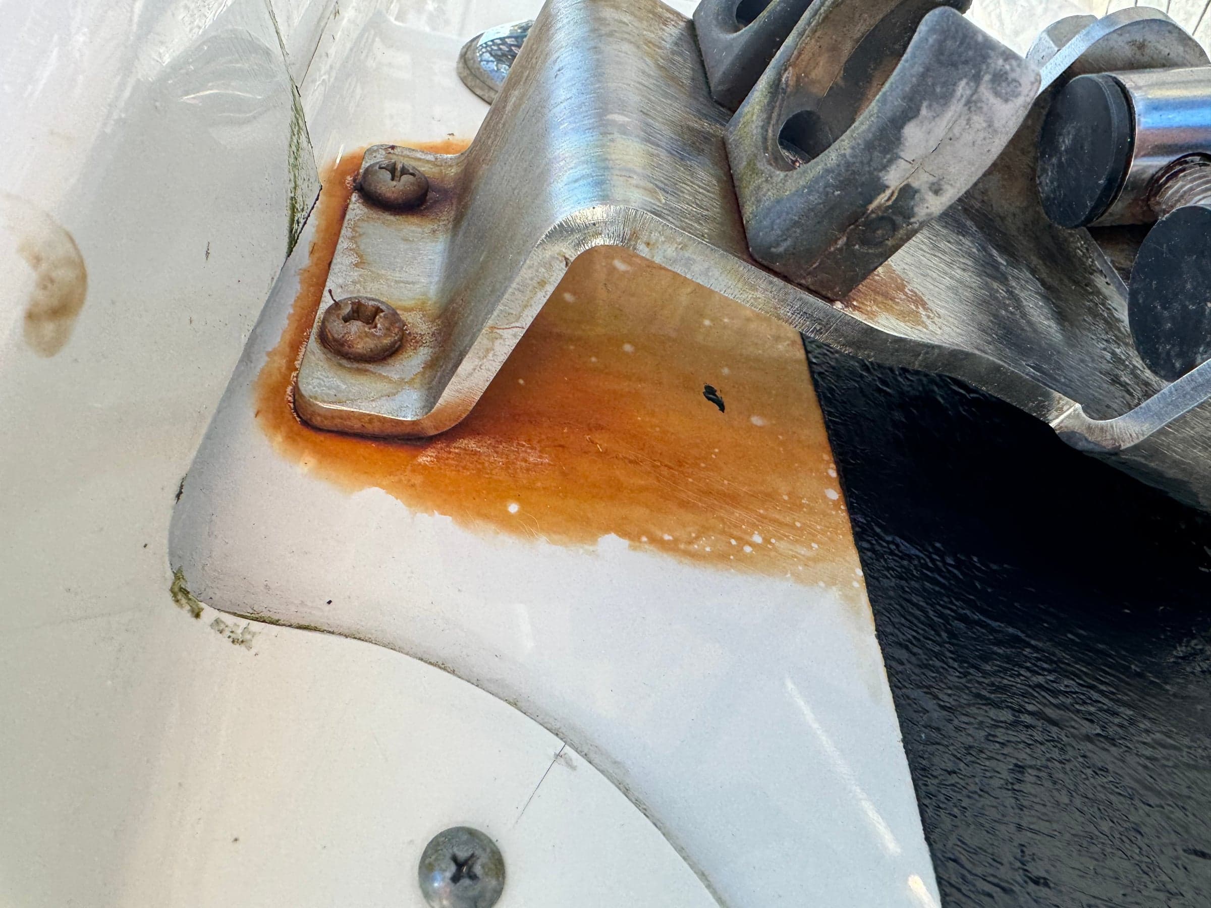Stainless trim-tab bracket on white hull with rust staining the gelcoat around fasteners